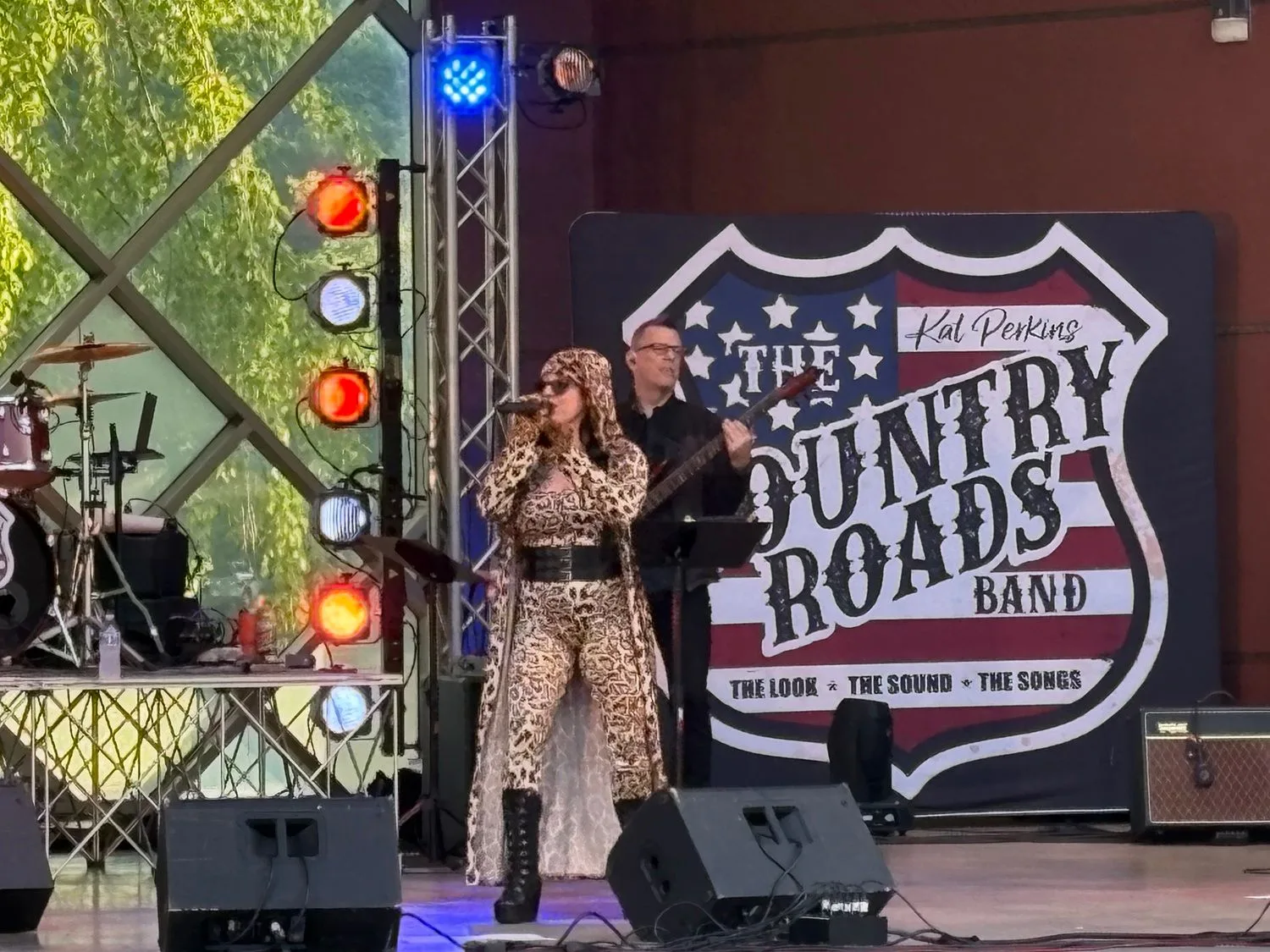 Country Roads performers on stage beside the band's red, white and blue banner in Bloomington