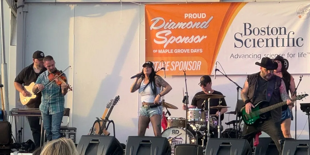 Kat Perkins and the Country Roads Band performing together at Maple Grove Days, with fiddle, guitars, bass and drums